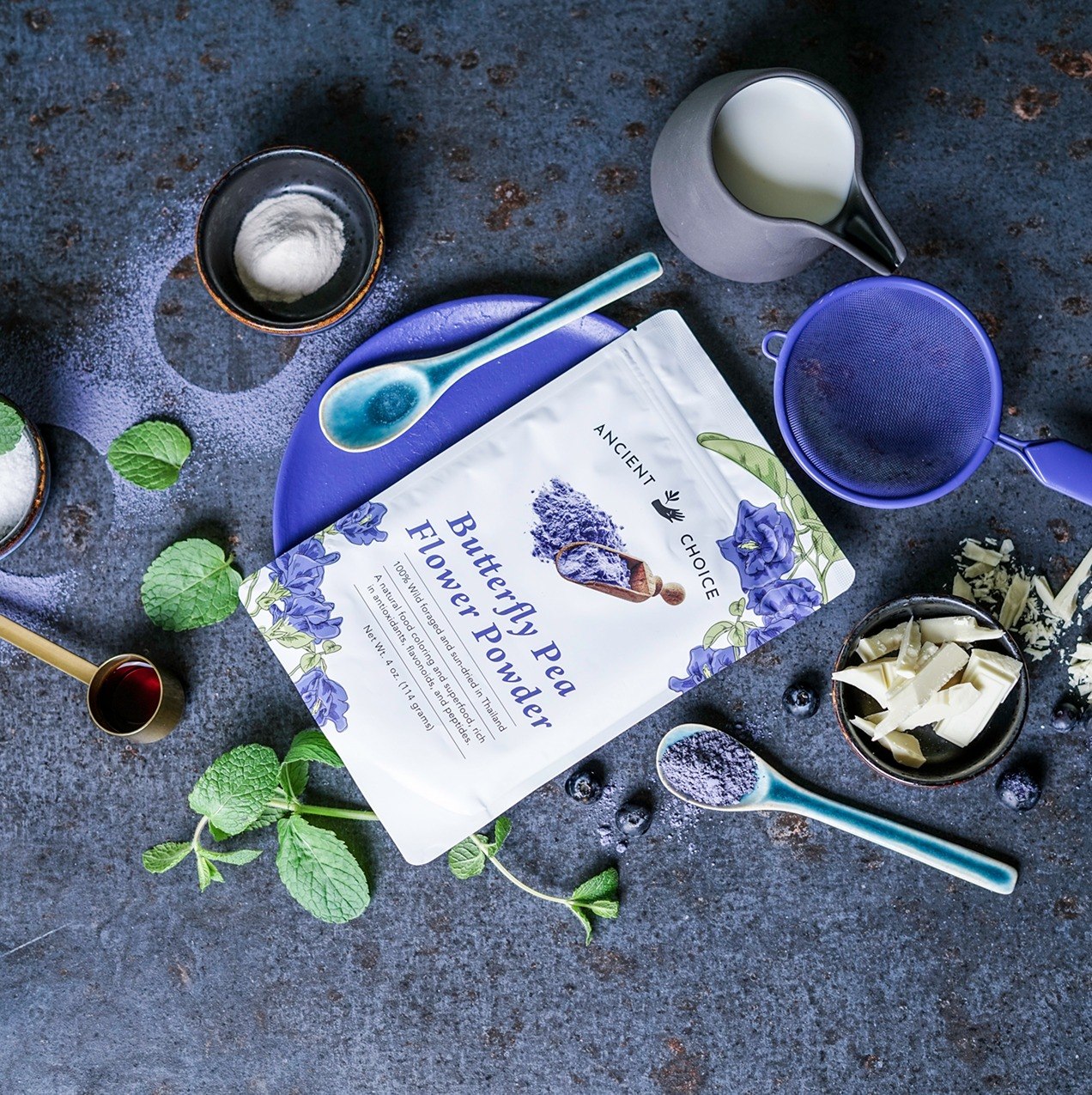 Butterfly Pea Flower Powder pouch on dark surface with spoons and blueberries